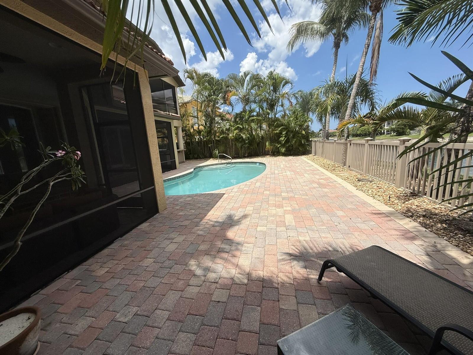 A backyard patio features brick pavers, a swimming pool, and a fence near palm trees — 3008 Hamblin Way, Wellington FL 33414, WELLINGTON, FL