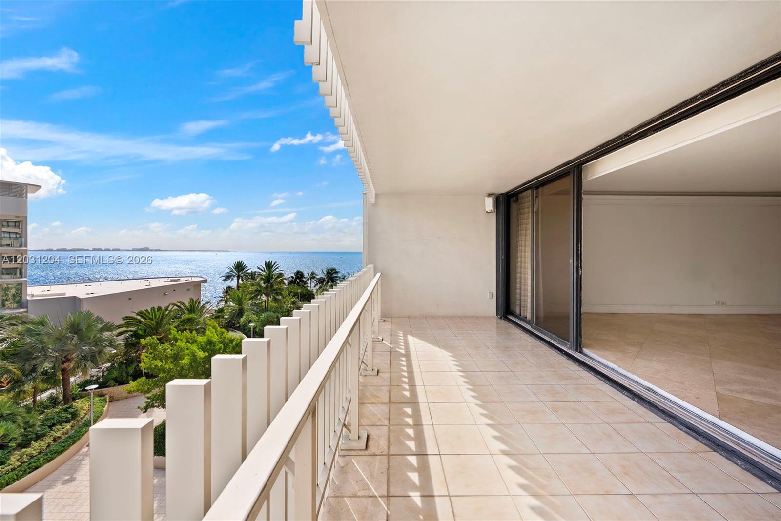 A balcony with a white railing overlooks the ocean and palm trees — 3 Grove Isle Dr # C605, Miami FL 33133, MIAMI, FL