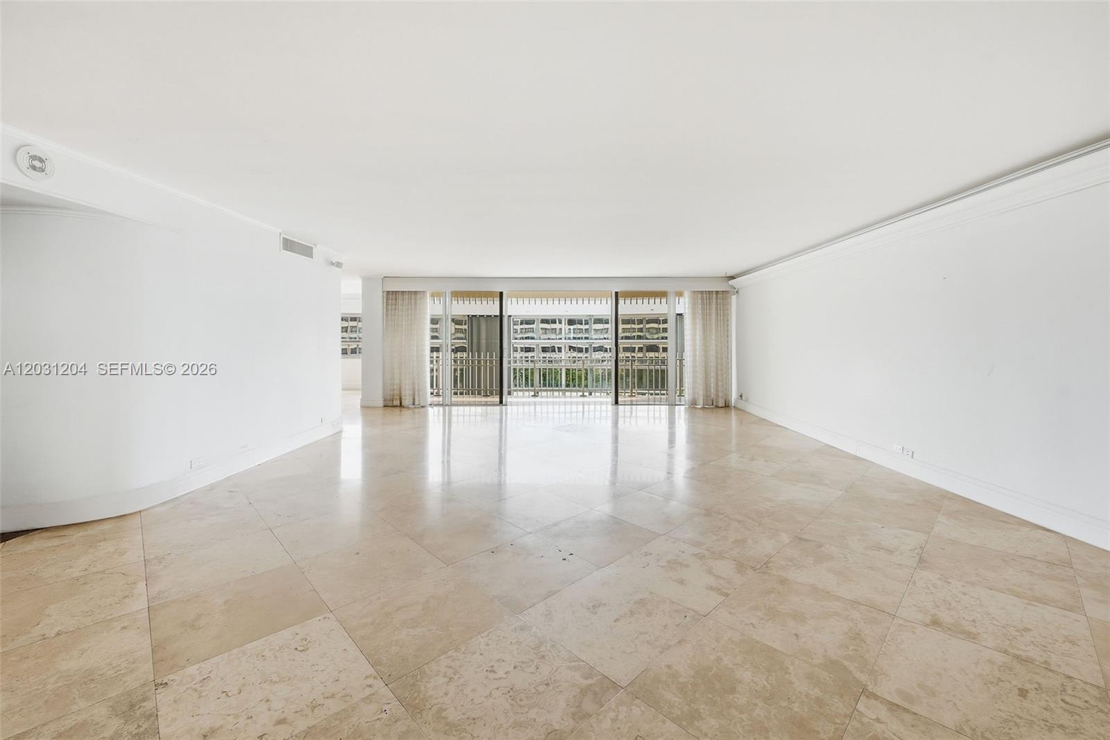 A spacious, empty room features light-colored tile flooring, white walls, and a large balcony entrance — 3 Grove Isle Dr # C605, Miami FL 33133, MIAMI, FL