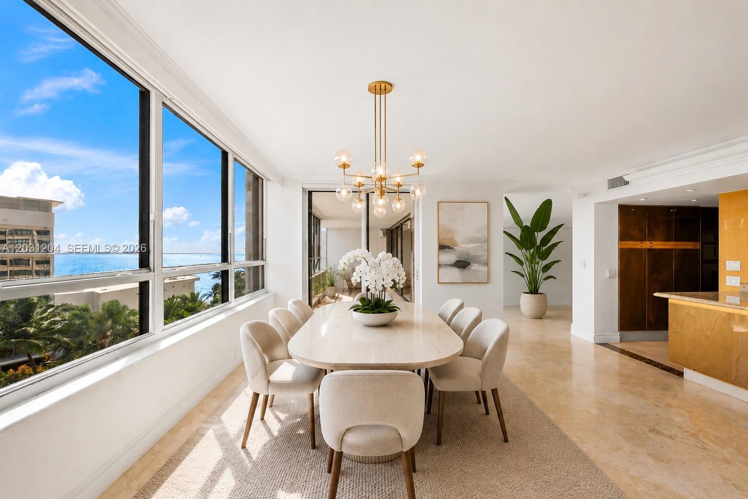 A dining room with a long table, modern chandelier, and floor-to-ceiling windows overlooking the ocean — 3 Grove Isle Dr # C605, Miami FL 33133, MIAMI, FL