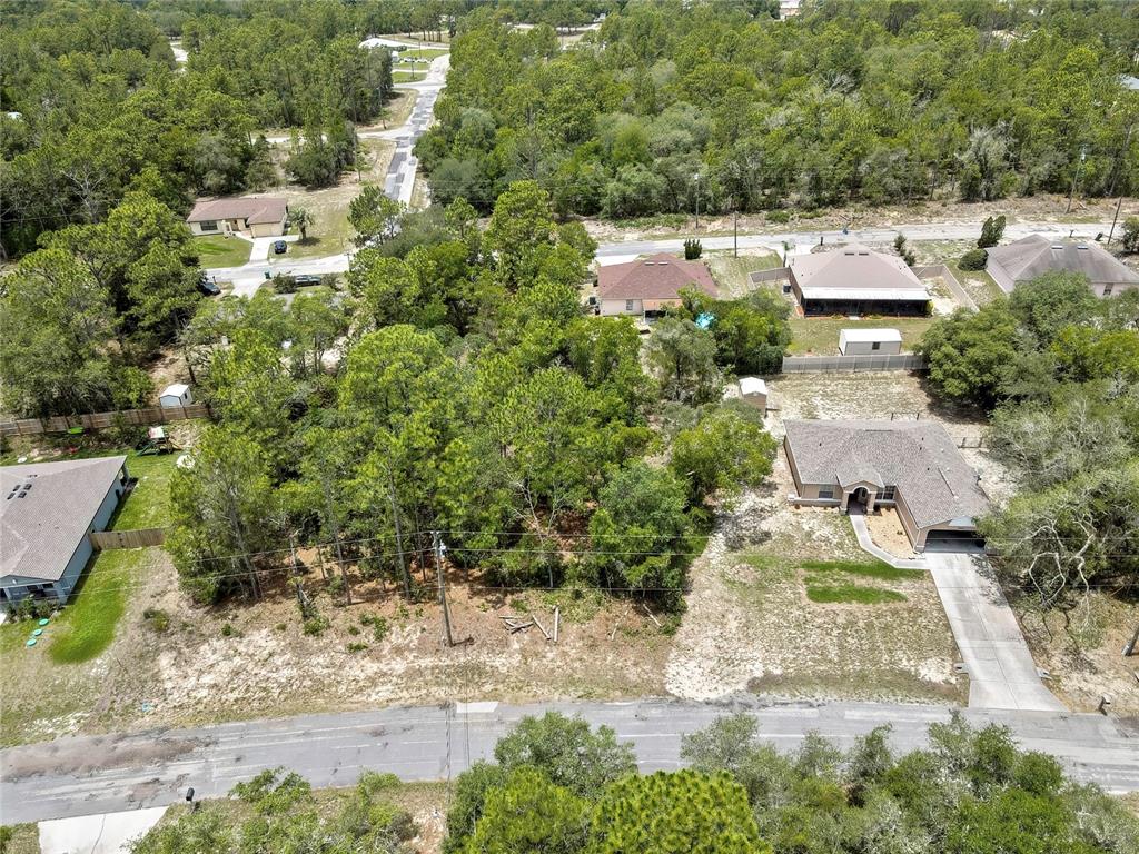 An aerial view shows a wooded residential lot situated between two houses and a road — 9652 N SAN JOSE WAY, CITRUS SPRINGS, FL