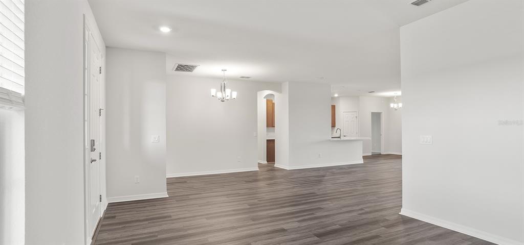 An open-concept living area features white walls, dark wood-look flooring, and a dining room chandelier — 5990 FRESHWATER CANYON DRIVE, ST CLOUD, FL