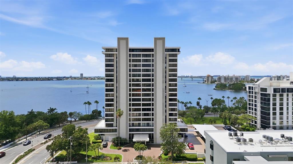 An aerial view shows a tall residential building situated along a waterfront with a bridge — 770 S PALM AVENUE UNIT 1501, SARASOTA, FL