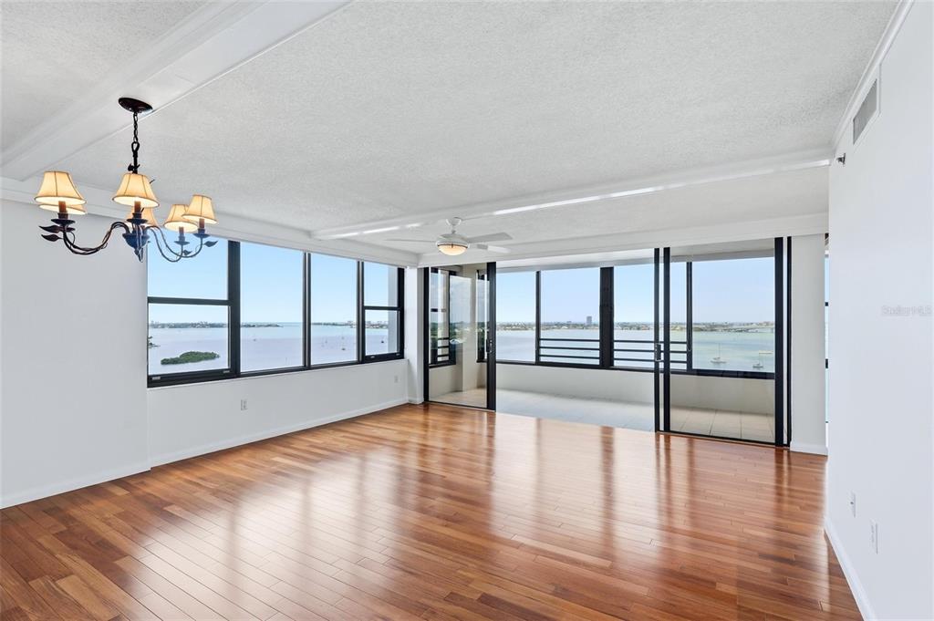A bright living room features hardwood floors, a chandelier, and floor-to-ceiling windows overlooking the water — 770 S PALM AVENUE UNIT 1501, SARASOTA, FL