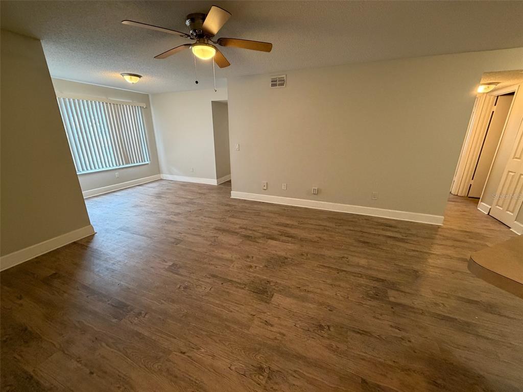 An empty living room features light-colored walls, wood-look flooring, and a ceiling fan — 4518 COMMANDER DRIVE UNIT 1921, ORLANDO, FL