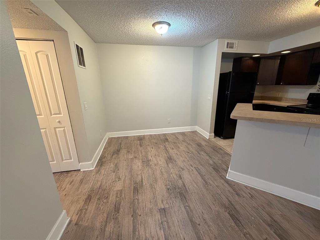 A dining area with wood-look flooring, light-colored walls, and an adjacent kitchen with dark cabinets — 4518 COMMANDER DRIVE UNIT 1921, ORLANDO, FL