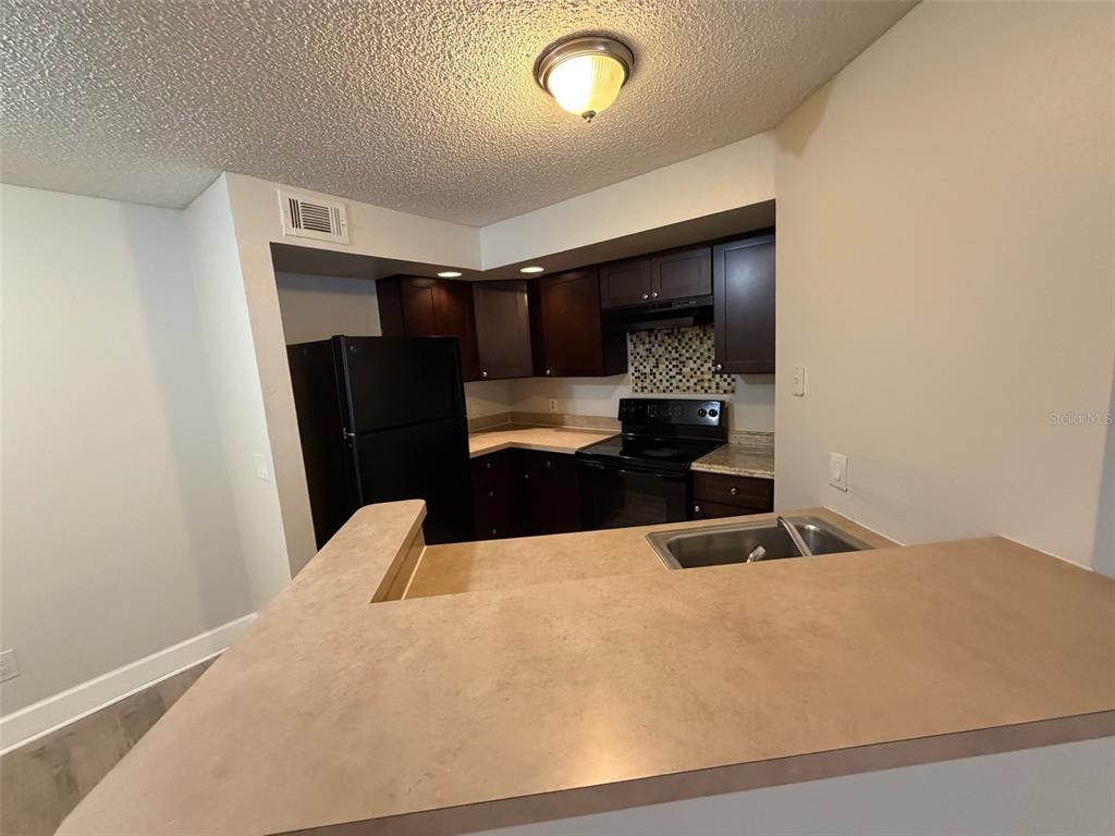A kitchen features dark wood cabinets, black appliances, a tiled backsplash, and a breakfast bar — 4518 COMMANDER DRIVE UNIT 1921, ORLANDO, FL