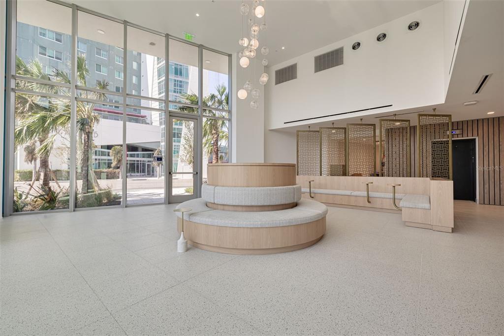 A modern lobby features a circular bench, floor-to-ceiling windows, and decorative gold room dividers — 777 3RD AVENUE N UNIT 1104, ST PETERSBURG, FL