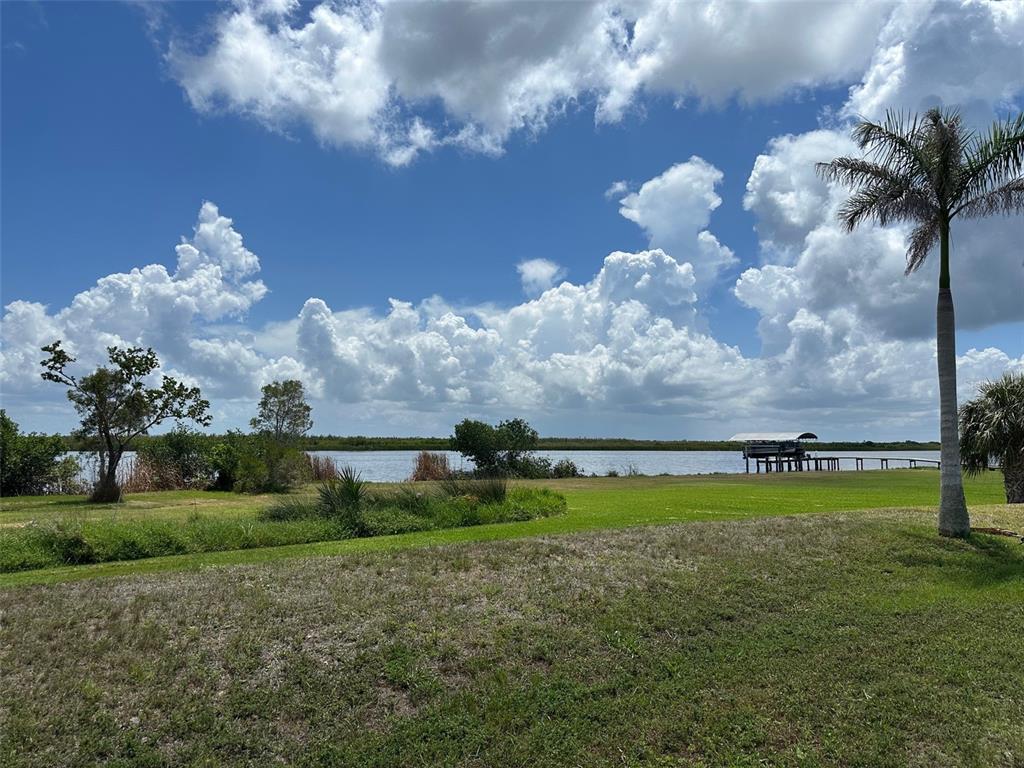 A grassy lawn leads to a waterfront view with a boat dock and palm tree — 10792 HATCHET CIRCLE, PORT CHARLOTTE, FL