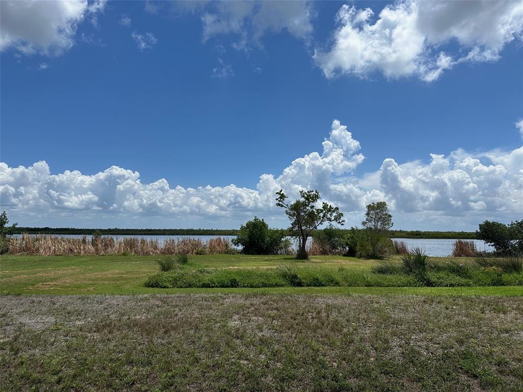 A grassy lawn leads to a body of water bordered by trees and tall grasses — 10792 HATCHET CIRCLE, PORT CHARLOTTE, FL