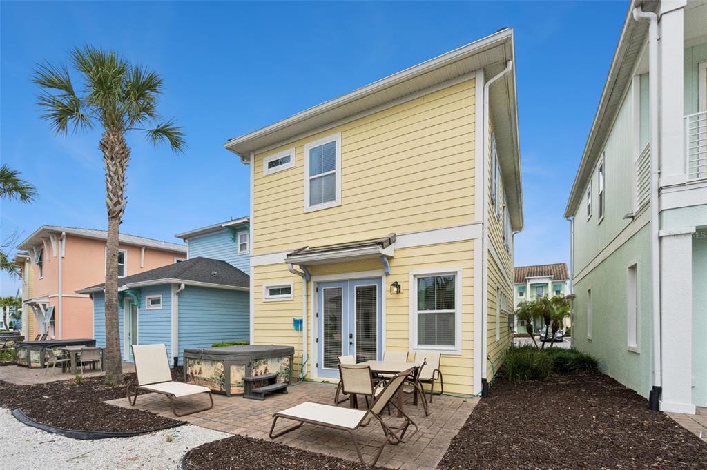 A yellow two-story house features a paved patio with lounge chairs and a hot tub — 8060 DREAMSICLE DRIVE, KISSIMMEE, FL