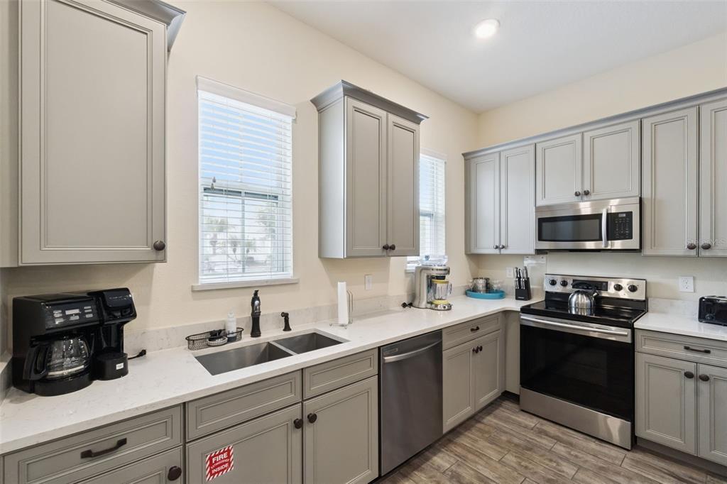 A kitchen features gray cabinets, stainless steel appliances, white countertops, and wood-look tile flooring — 8060 DREAMSICLE DRIVE, KISSIMMEE, FL