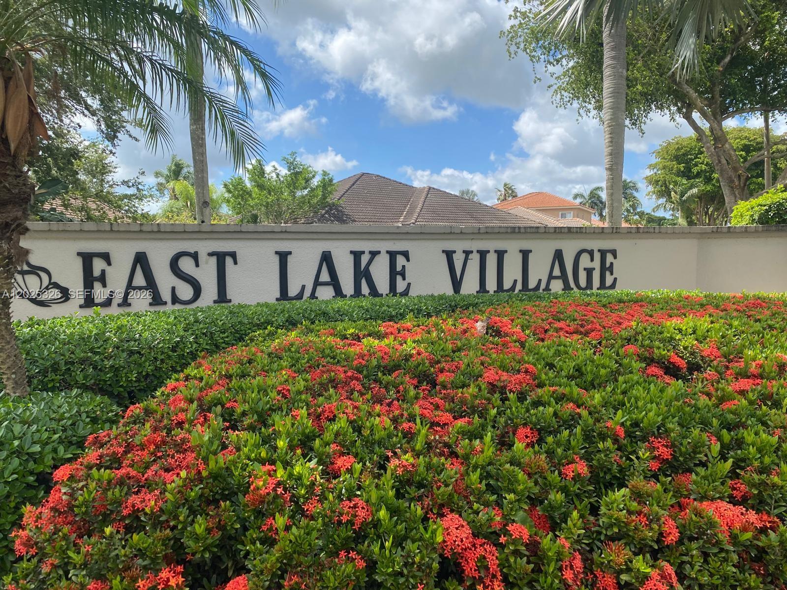 A sign for East Lake Village stands behind a large hedge of red flowers — 3035 SE 7th Pl, Homestead FL 33033, HOMESTEAD, FL