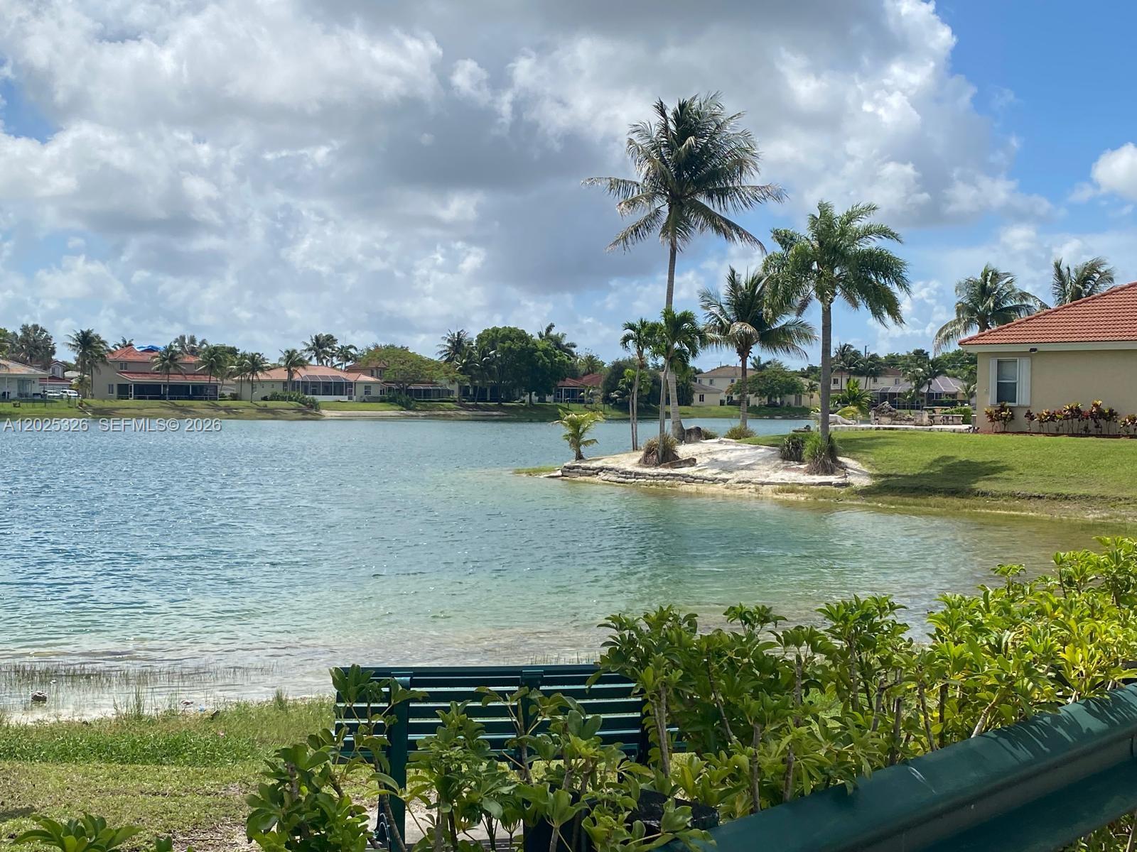 A view of a lake with a small sandy peninsula, palm trees, and a bench — 3035 SE 7th Pl, Homestead FL 33033, HOMESTEAD, FL