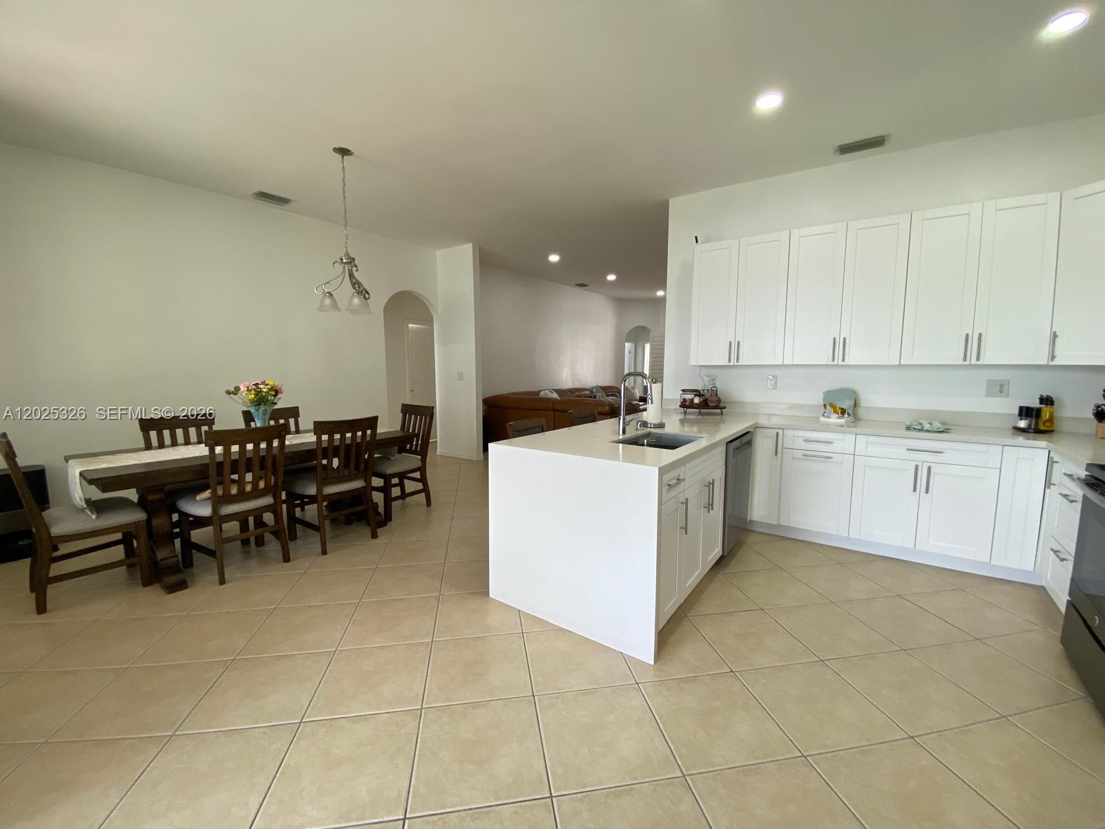 A kitchen with white cabinets and a central island flows into an adjacent dining area — 3035 SE 7th Pl, Homestead FL 33033, HOMESTEAD, FL