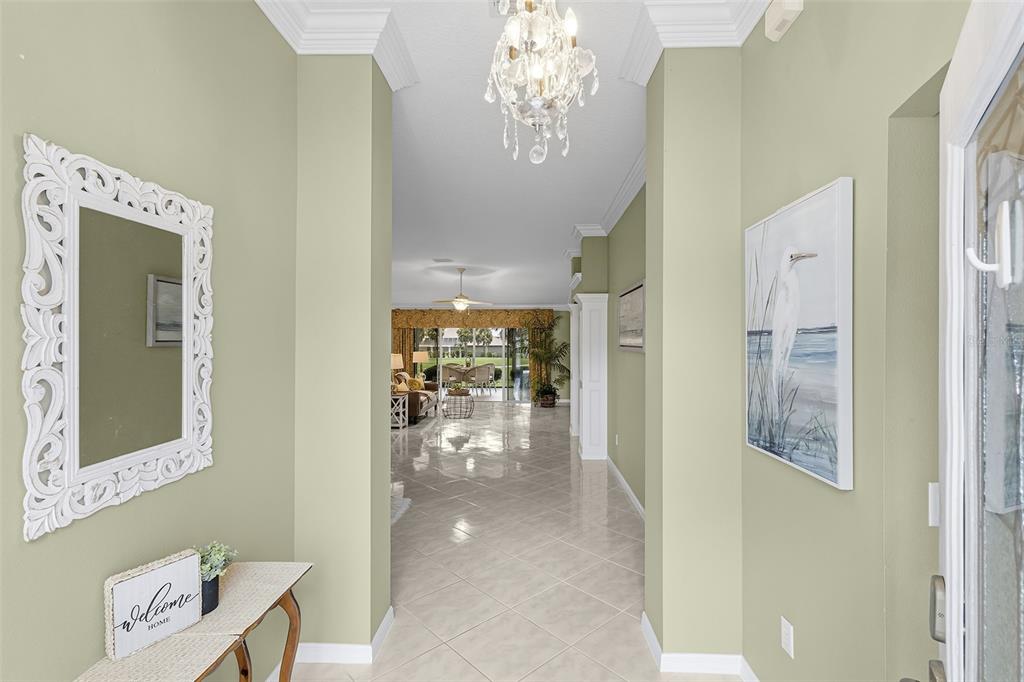 A bright foyer features light green walls, a crystal chandelier, and tile flooring — 1527 GOLDEN RIDGE DRIVE, THE VILLAGES, FL