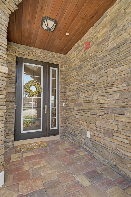 A stone-walled entryway features a dark wood front door, a wood-paneled ceiling, and paver flooring — 205 E VENICE AVENUE, VENICE, FL