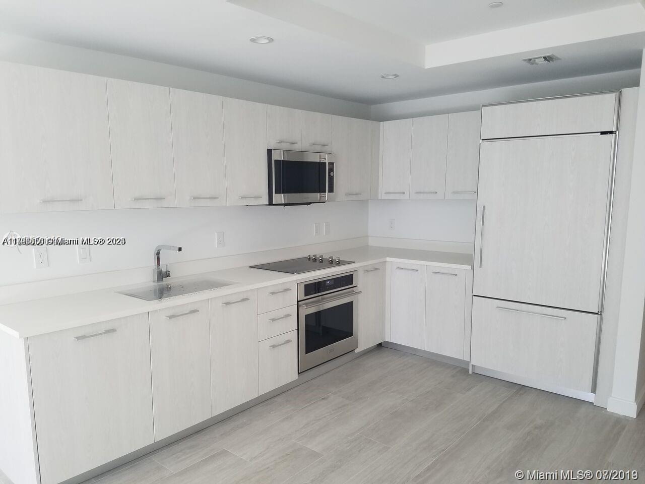 A modern kitchen features white flat-panel cabinetry, stainless steel appliances, and light wood-look flooring — 55 SW 9th St # 1805, Miami FL 33130, MIAMI, FL
