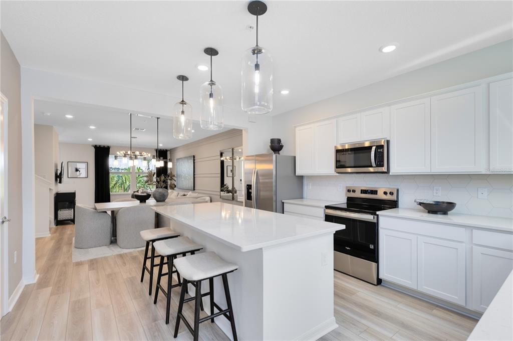 A modern kitchen features white cabinetry, a quartz island with bar stools, and stainless appliances — 6913 CREEK FALLS ALLEY, CLERMONT, FL