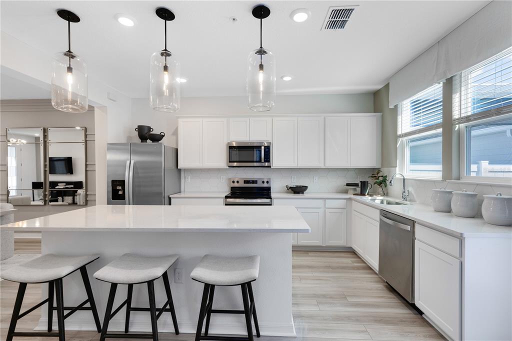 A modern kitchen features white cabinets, stainless steel appliances, a quartz island, and three barstools — 6913 CREEK FALLS ALLEY, CLERMONT, FL