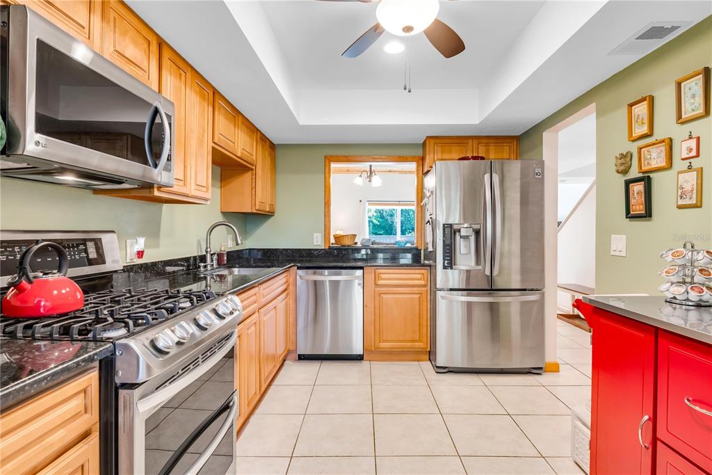 A kitchen features light wood cabinets, stainless steel appliances, dark countertops, and a tile floor — 702 GLASGOW COURT, WINTER SPRINGS, FL