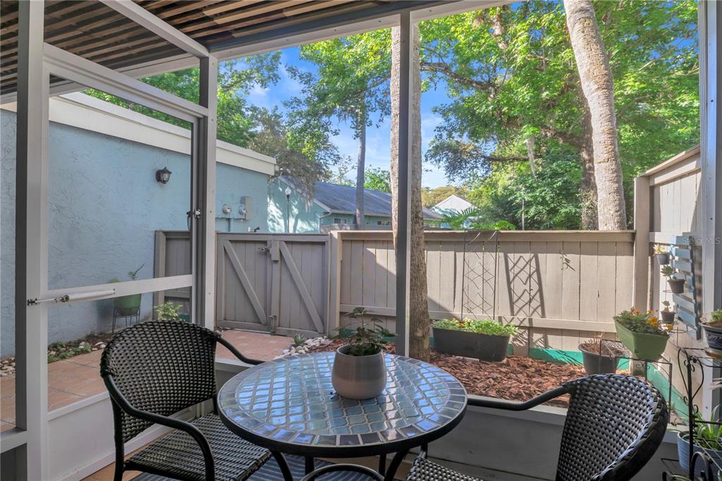 A screened-in patio features a mosaic-tiled table, two wicker chairs, and a wooden privacy fence — 702 GLASGOW COURT, WINTER SPRINGS, FL