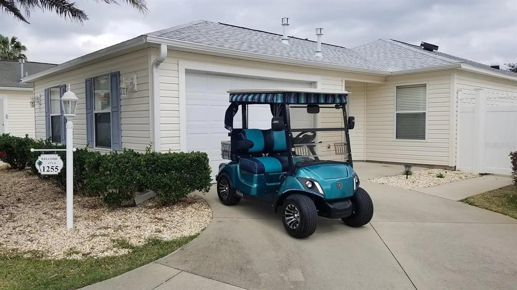 A teal golf cart is parked on the concrete driveway in front of a house — 1255 VIRGINIA DRIVE, THE VILLAGES, FL