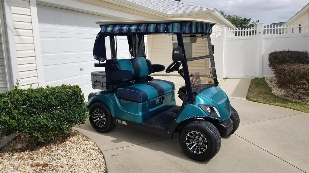 A teal Yamaha golf cart with a striped canopy is parked on a concrete driveway — 1255 VIRGINIA DRIVE, THE VILLAGES, FL