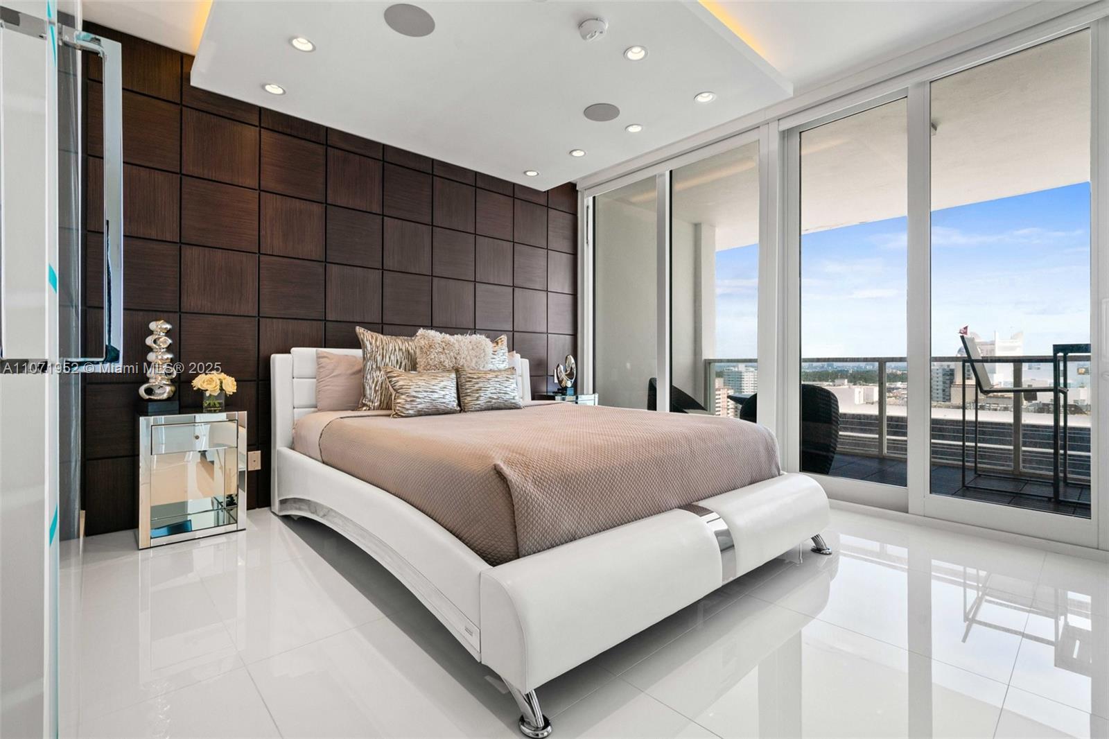 A modern bedroom features a white bed, dark wood wall panels, and floor-to-ceiling glass doors — 100 Lincoln Rd, Miami Beach FL 33139, MIAMI BEACH, FL