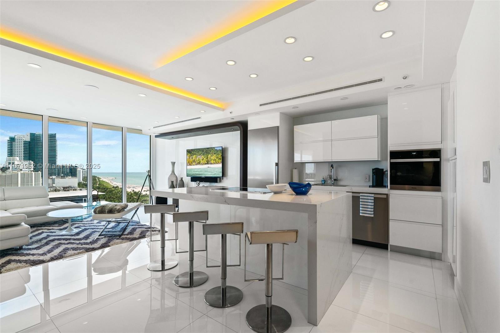 A modern kitchen with a marble island and bar stools overlooks a coastal living area — 100 Lincoln Rd, Miami Beach FL 33139, MIAMI BEACH, FL