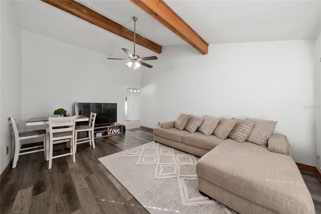 A living room with wood-look flooring, vaulted ceilings, exposed beams, and a ceiling fan — 115 TOLUCA DRIVE, KISSIMMEE, FL