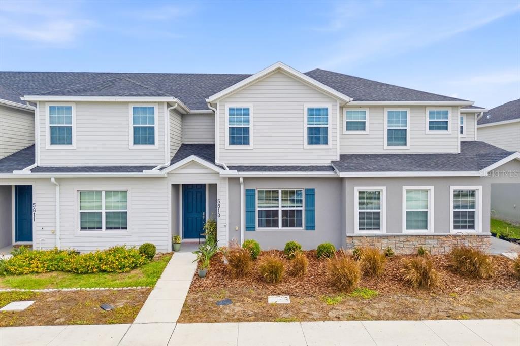A two-story townhouse with light siding, a blue front door, and a concrete walkway — 5813 MILLHOUSE WAY, ST CLOUD, FL