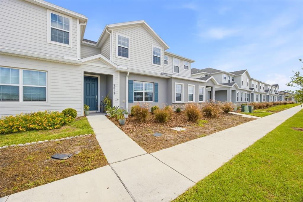 A bright entryway features a white door, light wood flooring, a mirror, and potted plants — 5813 MILLHOUSE WAY, ST CLOUD, FL