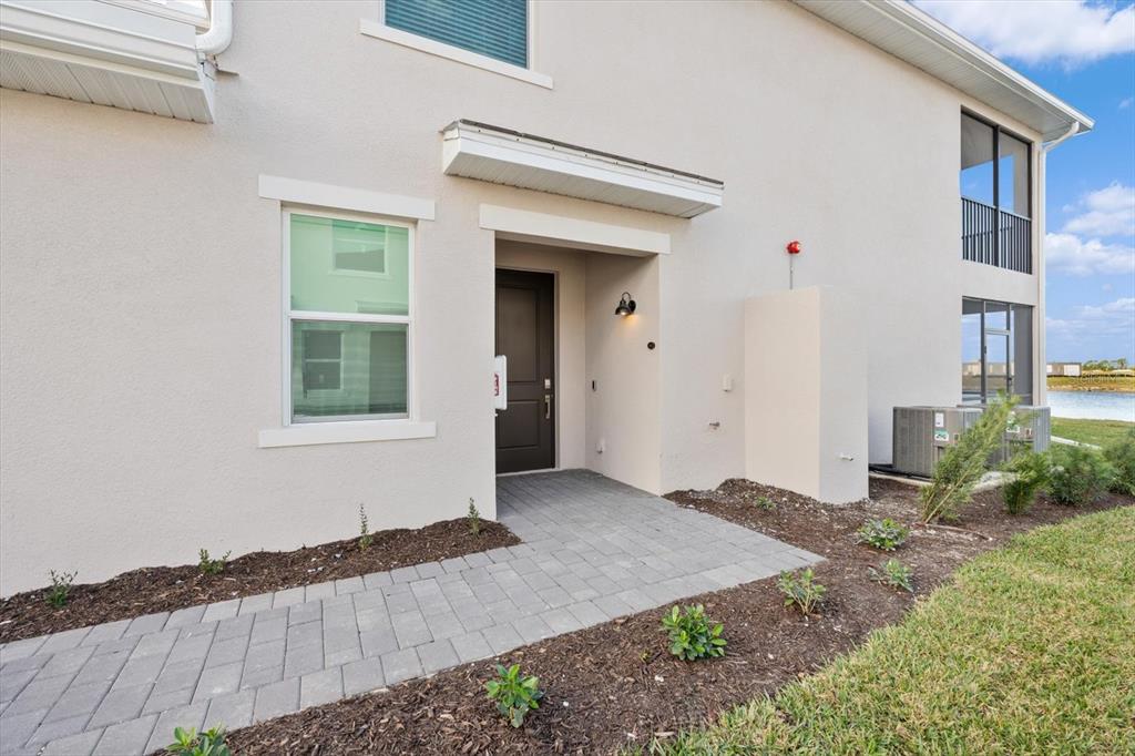 A paved walkway leads to the dark front door of a beige two-story townhouse — 17585 BORACAY COURT UNIT 2-102, VENICE, FL