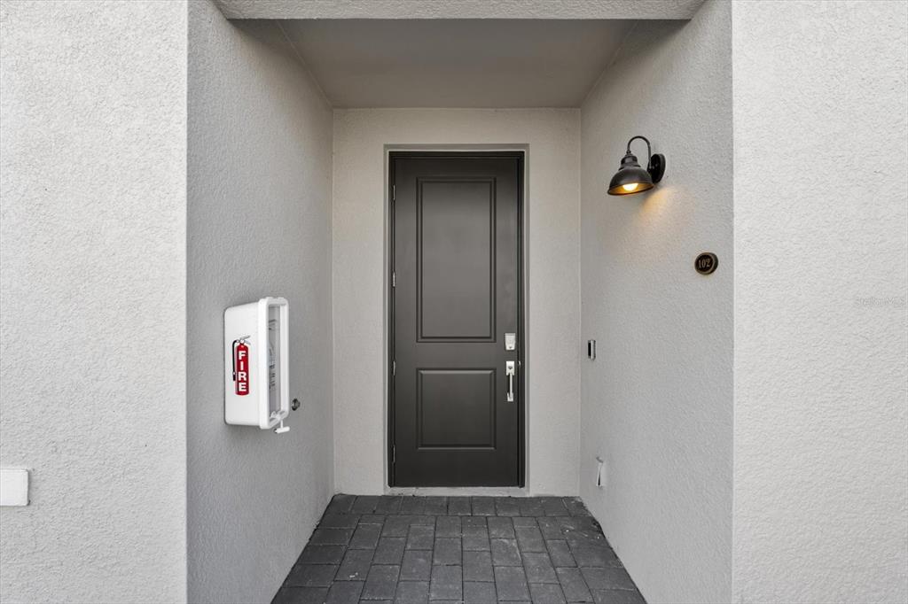 A dark gray front door is set in a recessed entryway with a fire extinguisher box — 17585 BORACAY COURT UNIT 2-102, VENICE, FL