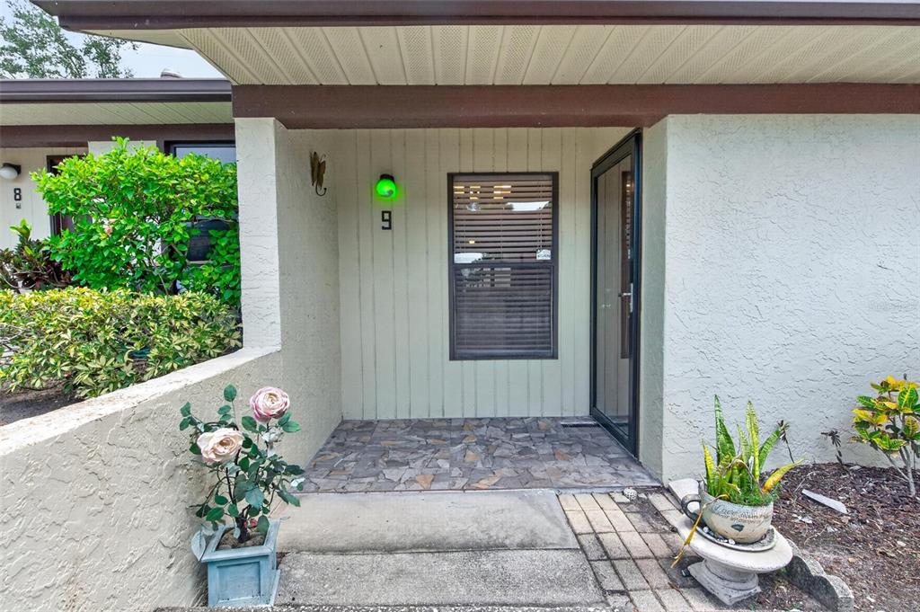 The exterior entrance of a home features a stone-tiled porch, a window, and potted plants — 1311 POWDERPUFF DRIVE UNIT 1009, DUNEDIN, FL