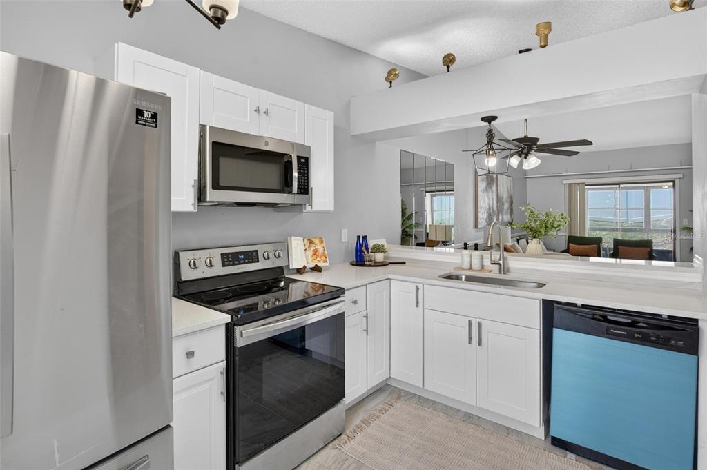 A kitchen features white cabinets, stainless steel appliances, and a pass-through window to the living area — 1311 POWDERPUFF DRIVE UNIT 1009, DUNEDIN, FL