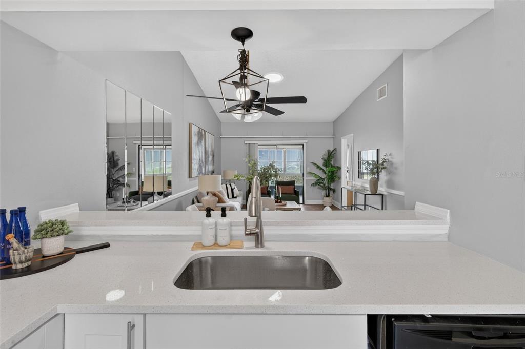 A kitchen sink and countertop look out into a living room with a ceiling fan — 1311 POWDERPUFF DRIVE UNIT 1009, DUNEDIN, FL