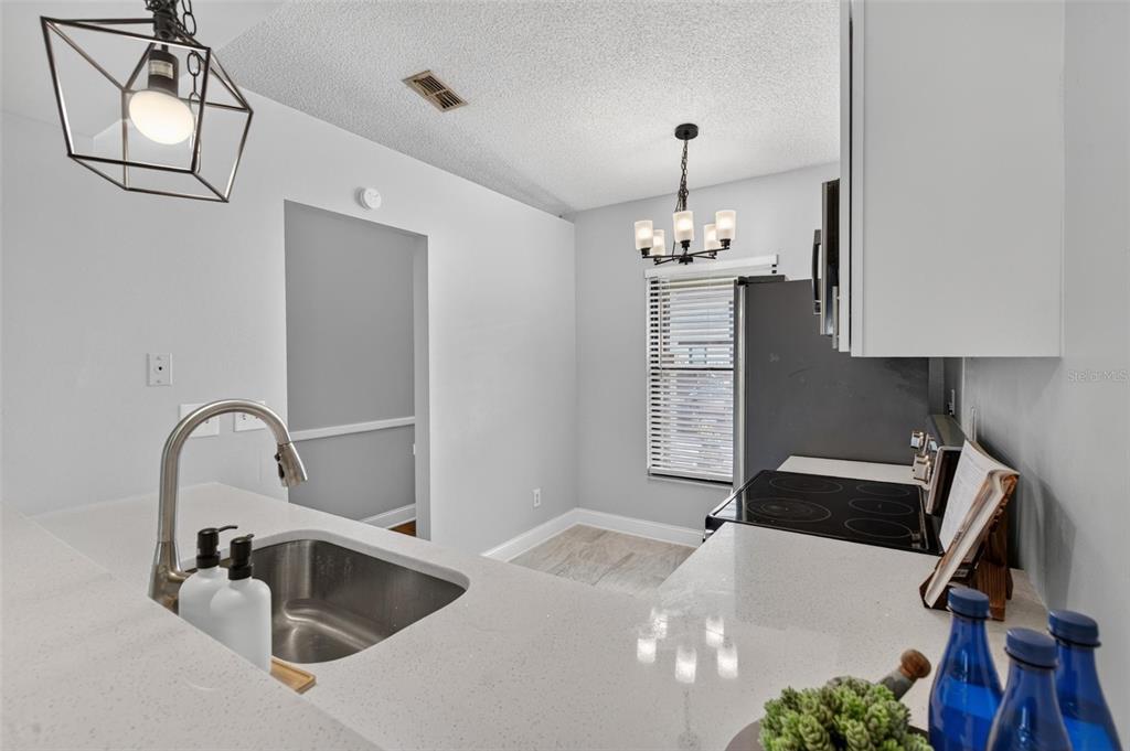 A kitchen features white countertops, a stainless steel sink, and a dining area with lighting — 1311 POWDERPUFF DRIVE UNIT 1009, DUNEDIN, FL