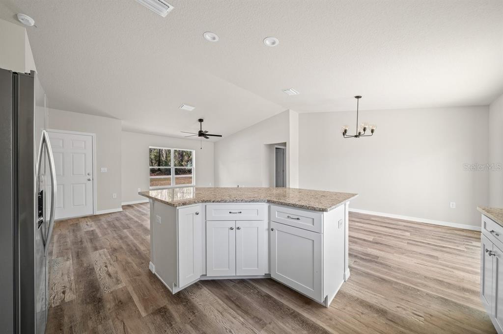A kitchen island with granite countertops sits in an open-concept room with wood-look flooring — 8992 N LISA TERRACE, CITRUS SPRINGS, FL