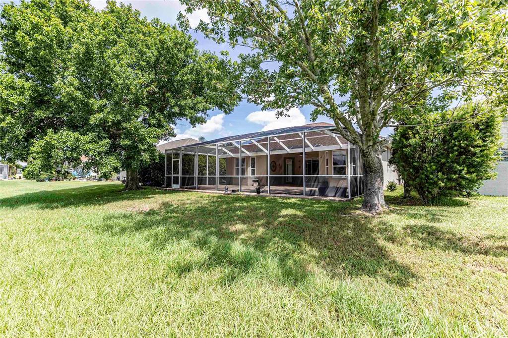 A backyard view of a house with a screened-in patio and large mature trees — 12104 SE 178TH STREET, SUMMERFIELD, FL