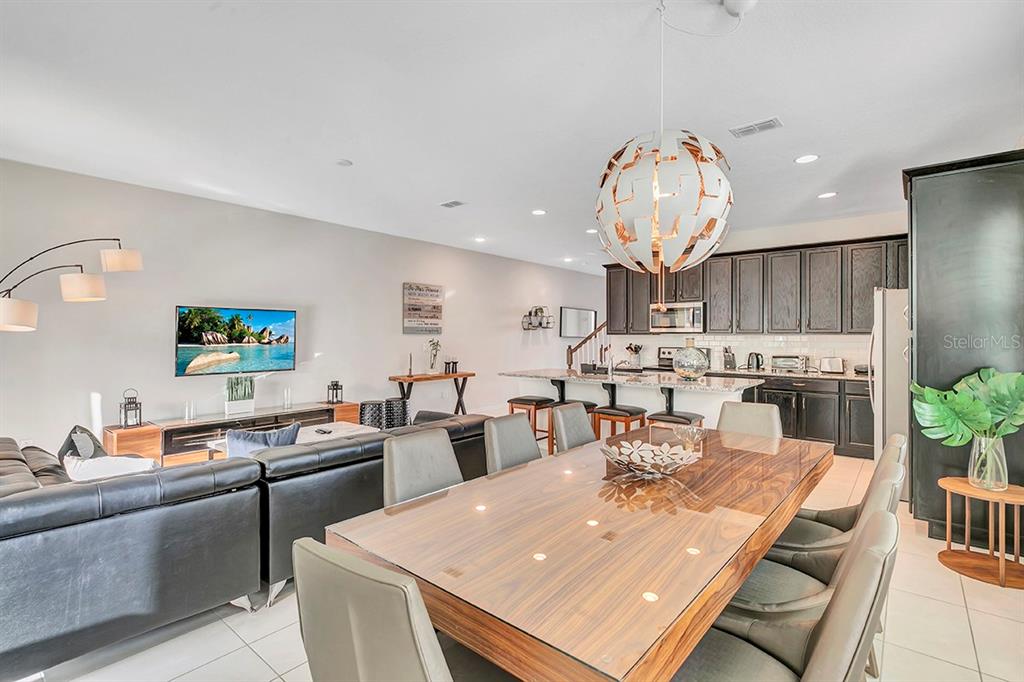 An open-concept living and dining area features dark cabinetry, a large pendant light, and tile flooring — 1532 CAREY PALM CIRCLE, KISSIMMEE, FL