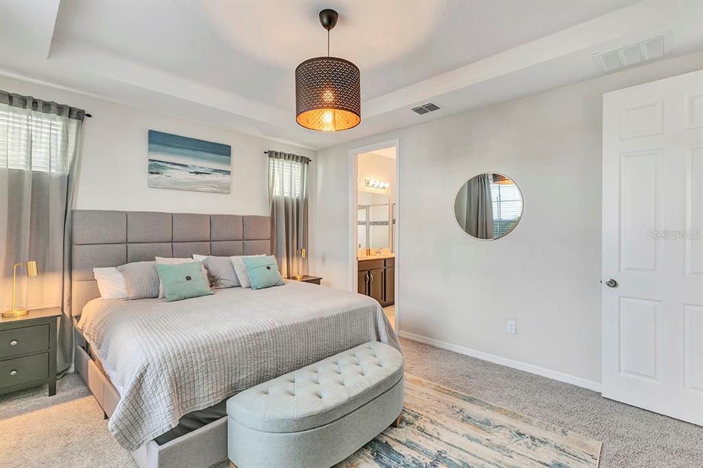 A bedroom features a gray upholstered bed, a tufted bench, and a circular wall mirror — 1532 CAREY PALM CIRCLE, KISSIMMEE, FL