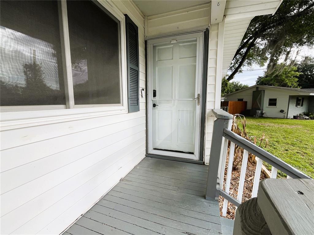 A white front door with a storm door opens onto a gray wooden porch — 121 MARIS COURT, LAKELAND, FL