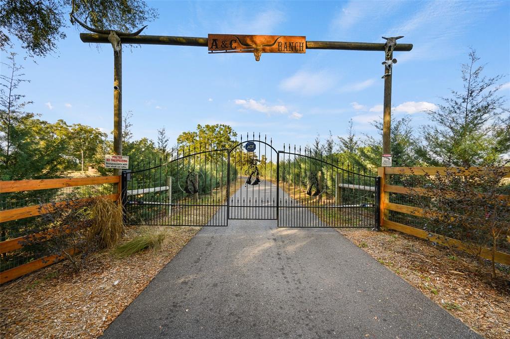 A paved driveway leads through a black metal gate beneath an A&C Ranch sign — 22928 NW 102ND AVENUE, ALACHUA, FL