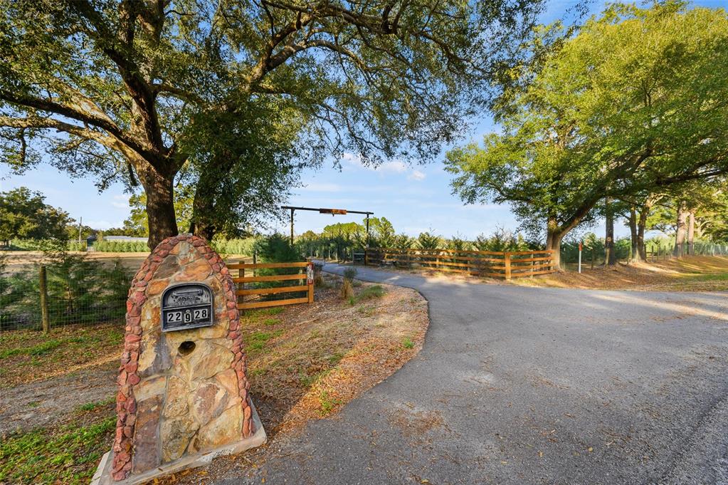 A stone mailbox stands at the entrance of a paved driveway leading to a wooden gate — 22928 NW 102ND AVENUE, ALACHUA, FL
