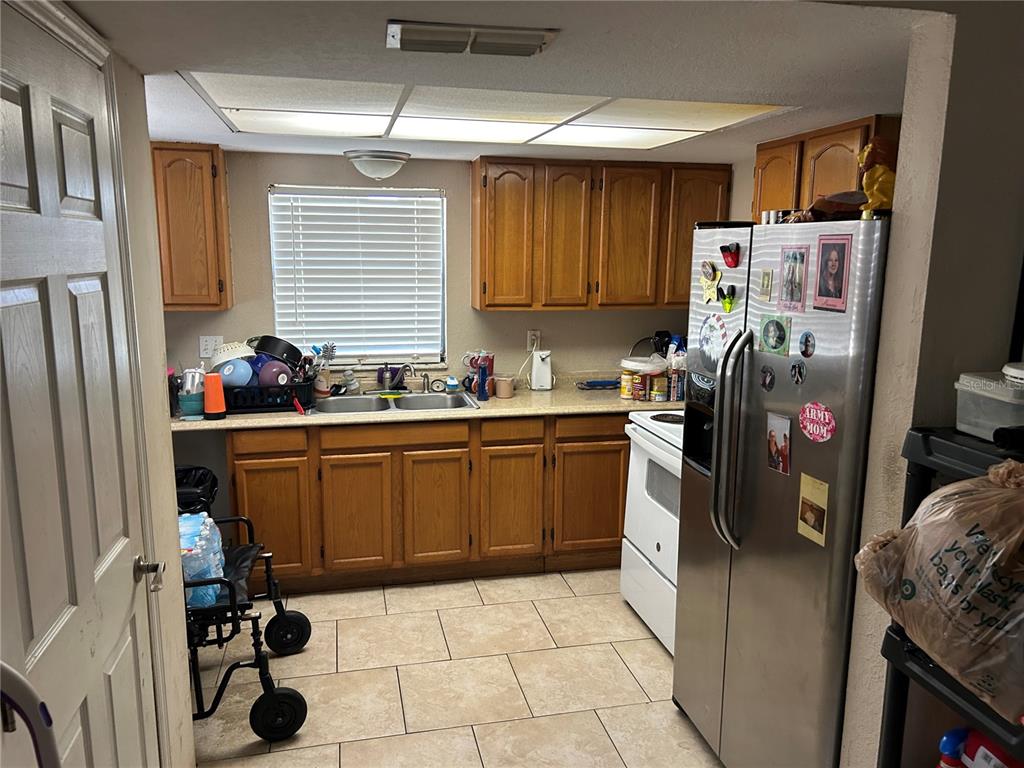 A kitchen features wood cabinets, tile flooring, a stainless steel refrigerator, and a double sink — 6301 58TH STREET N UNIT 304, PINELLAS PARK, FL