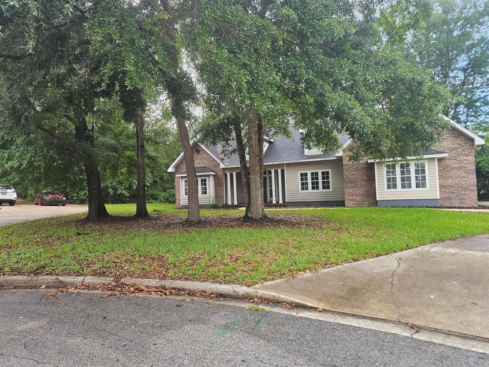 A single-story brick and siding house sits behind several large trees on a grassy lot — 11444 NW 18th Lane, Gainesville FL 32606, GAINESVILLE, FL