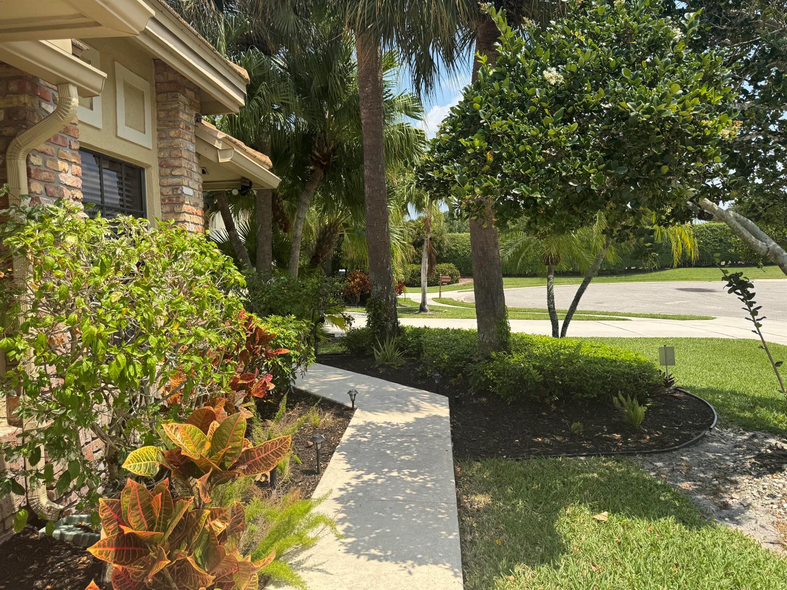A concrete walkway leads past a brick house and lush landscaping toward a suburban street — 6803 Bitterbush Place, Boynton Beach FL 33472, BOYNTON BEACH, FL