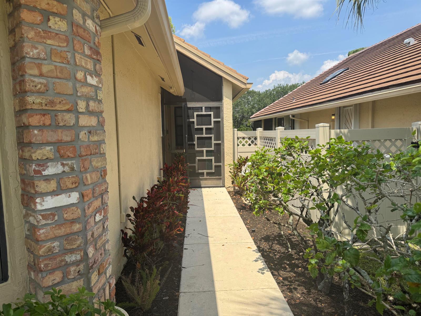 A concrete walkway leads to a screened entryway between two houses with landscaped garden beds — 6803 Bitterbush Place, Boynton Beach FL 33472, BOYNTON BEACH, FL